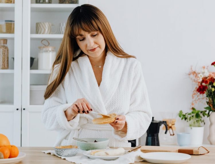 A woman in a bathrobe preparing breakfast in a home kitchen.
